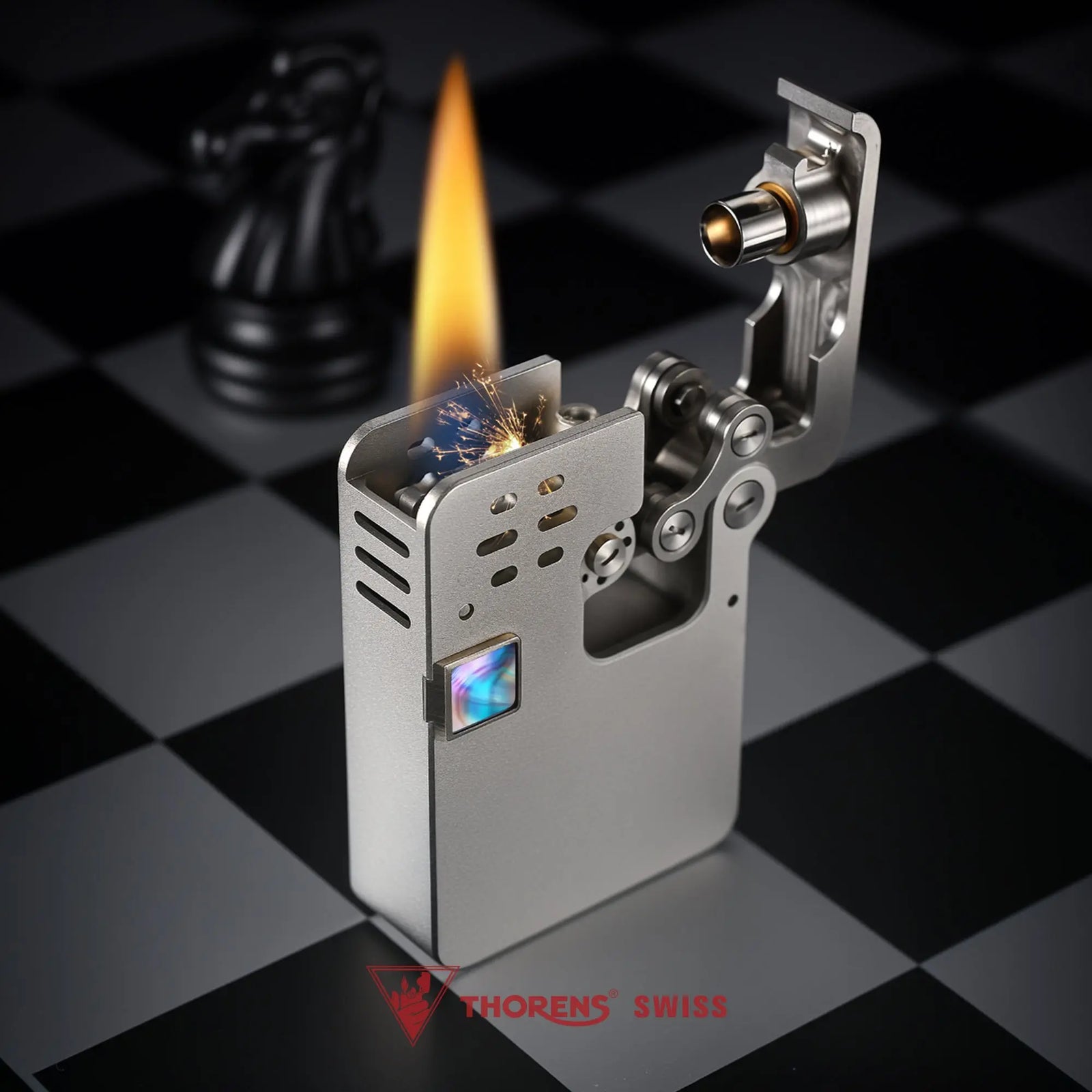 A brushed grey Ejection Lighter in an open, ignited state with a bright flame and visible sparks, showcasing its complex internal linkages and hollowing machine frame.