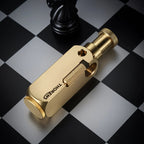 A brushed brass Flamido lighter with a unique octagonal body, featuring the Thorens logo and a knurled plunger, resting on a black and white chessboard.