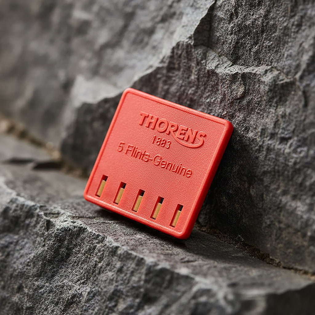Thorens genuine lighter flint pack leaning against a textured stone surface, showing the red branded case with five replacement flints for mechanical lighter maintenance