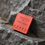 Thorens genuine lighter flint pack leaning against a textured stone surface, showing the red branded case with five replacement flints for mechanical lighter maintenance