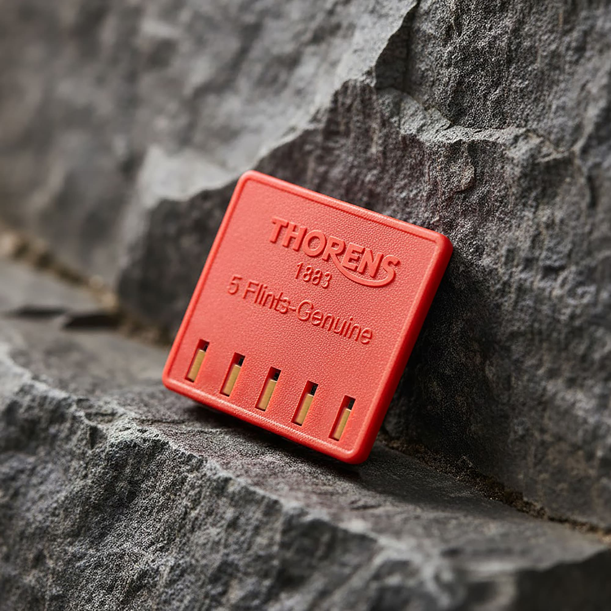 Thorens genuine lighter flint pack leaning against a textured stone surface, showing the red branded case with five replacement flints for mechanical lighter maintenance