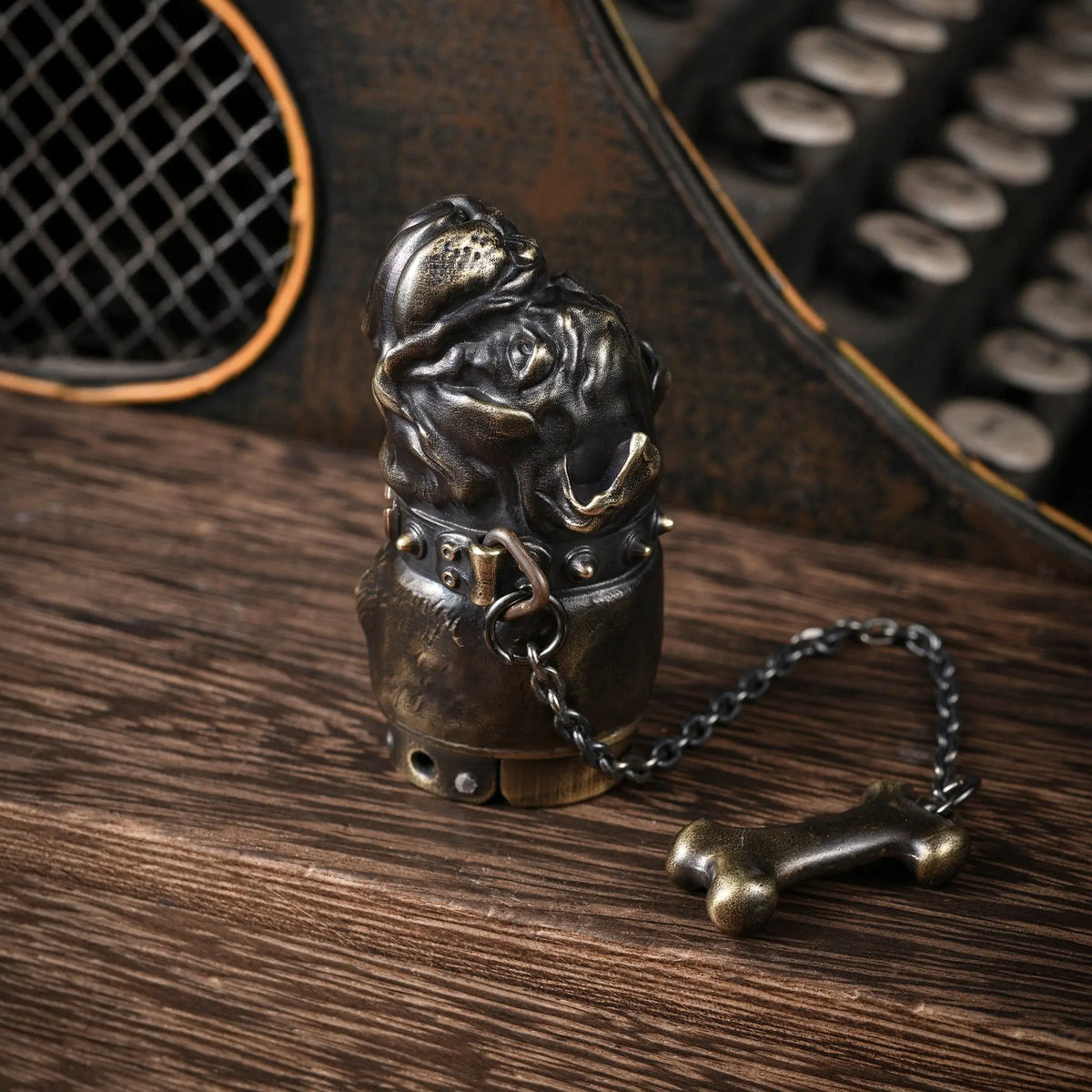 A vertical view of the Thorens French Bulldog lighter in antique brass, standing on a wooden surface to highlight the intricate facial details, spiked collar, and chain-linked bone charm.