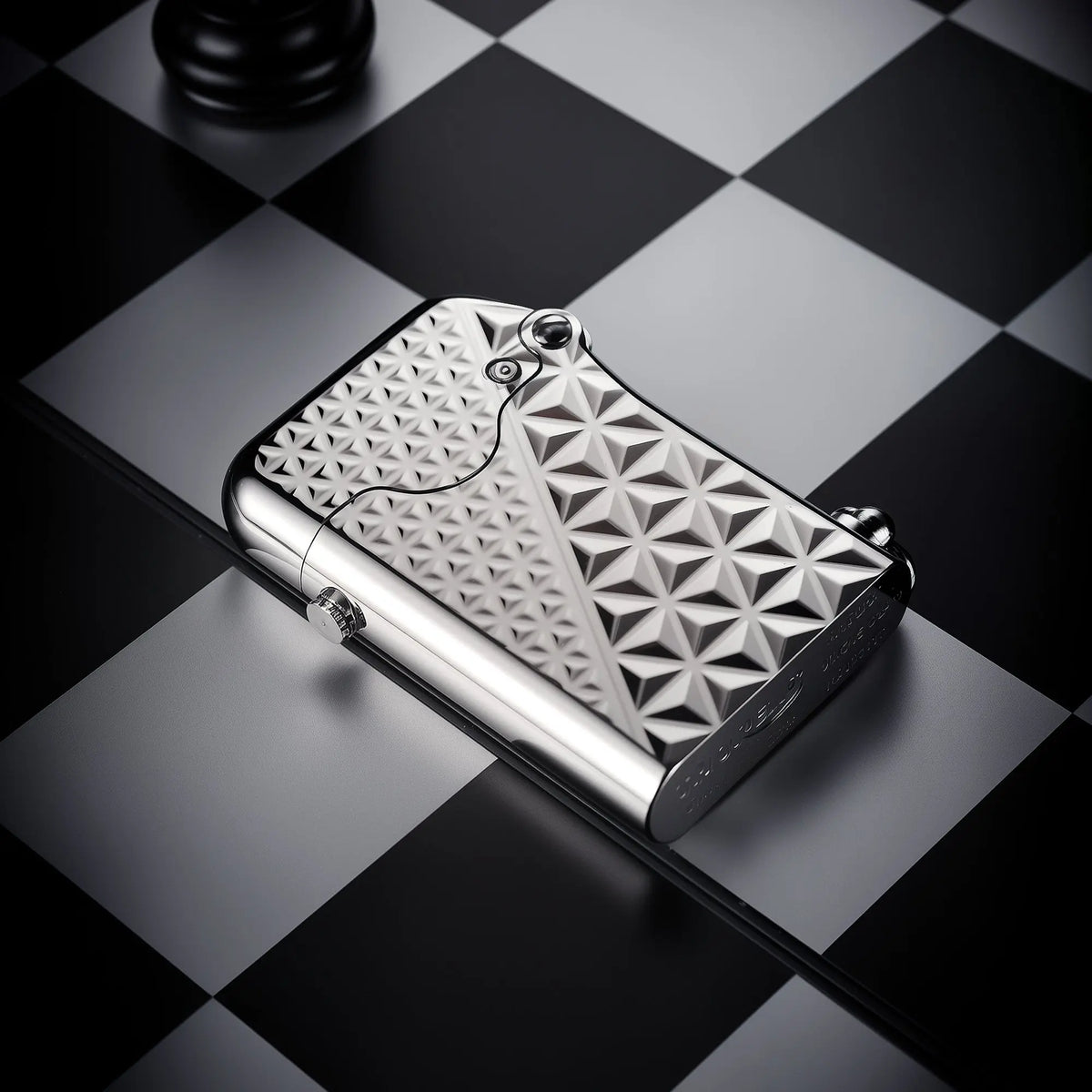 A silver-plated Thorens Gen 1 single claw lighter with a geometric diamond pattern engraving, resting on a checkered surface.