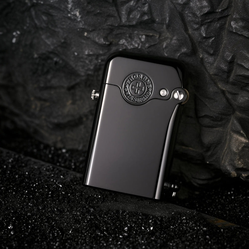 A glossy black Gen 1 Single Claw lighter resting against a dark textured stone background, featuring the embossed Thorens Swiss Brand emblem.