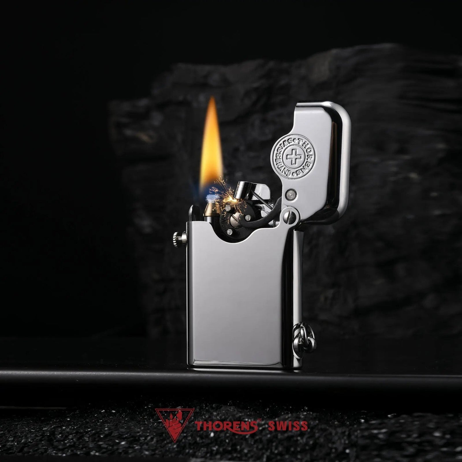 An ignited Thorens Gen 1 Single Claw silver lighter with brand emblem, displaying a vibrant flame and mechanical sparks against a dramatic dark rock background.