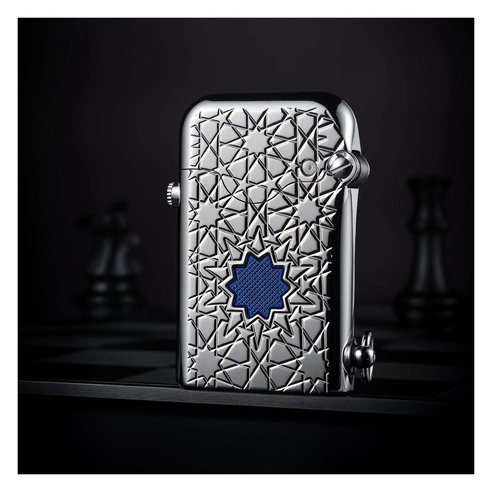 A vertical view of the Thorens Single Claw Gen 1 lighter featuring a polished silver body with star engravings and a centered blue lucky star inlay, standing on a dark chessboard.