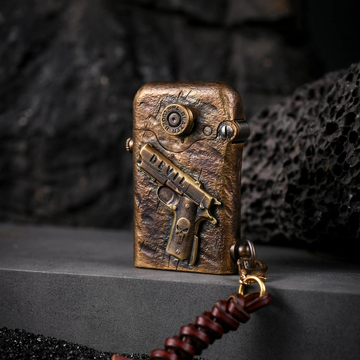Hand-carved brass Thorens lighter featuring a 1911 pistol relief and Punisher skull detail, displayed on a dark volcanic rock background.