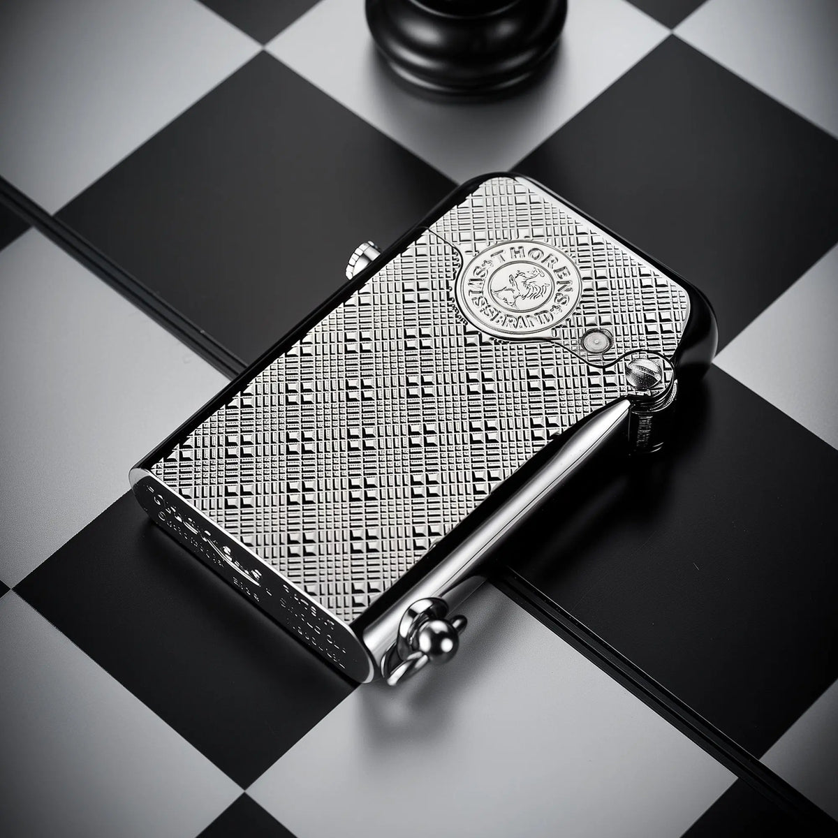 A silver Thorens Gen 1 single claw lighter with an engraved plum pattern lying on a black and white chessboard, showcasing its refined EDC aesthetics.