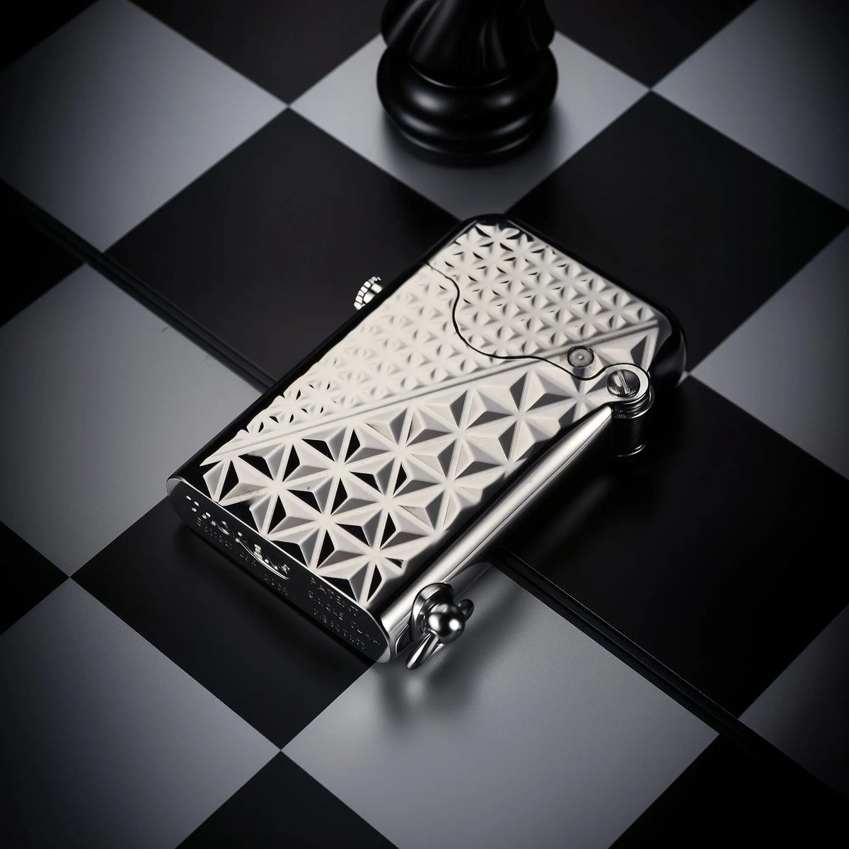 A silver-finished Thorens Gen 1 single claw lighter with a diamond pattern engraving, lying horizontally on a black and white chessboard.