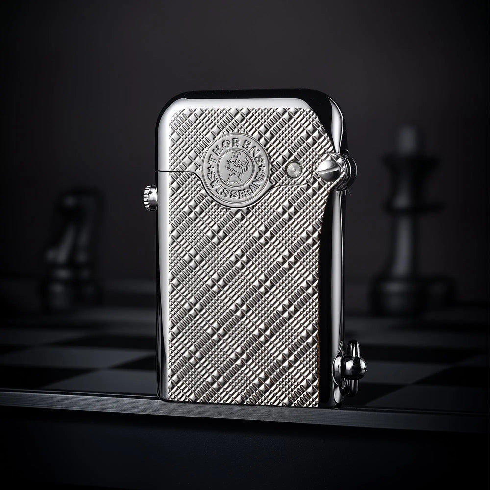 A silver Thorens Gen 1 single claw lighter featuring an intricate engraved plum pattern and heritage brand emblem on a chessboard surface.