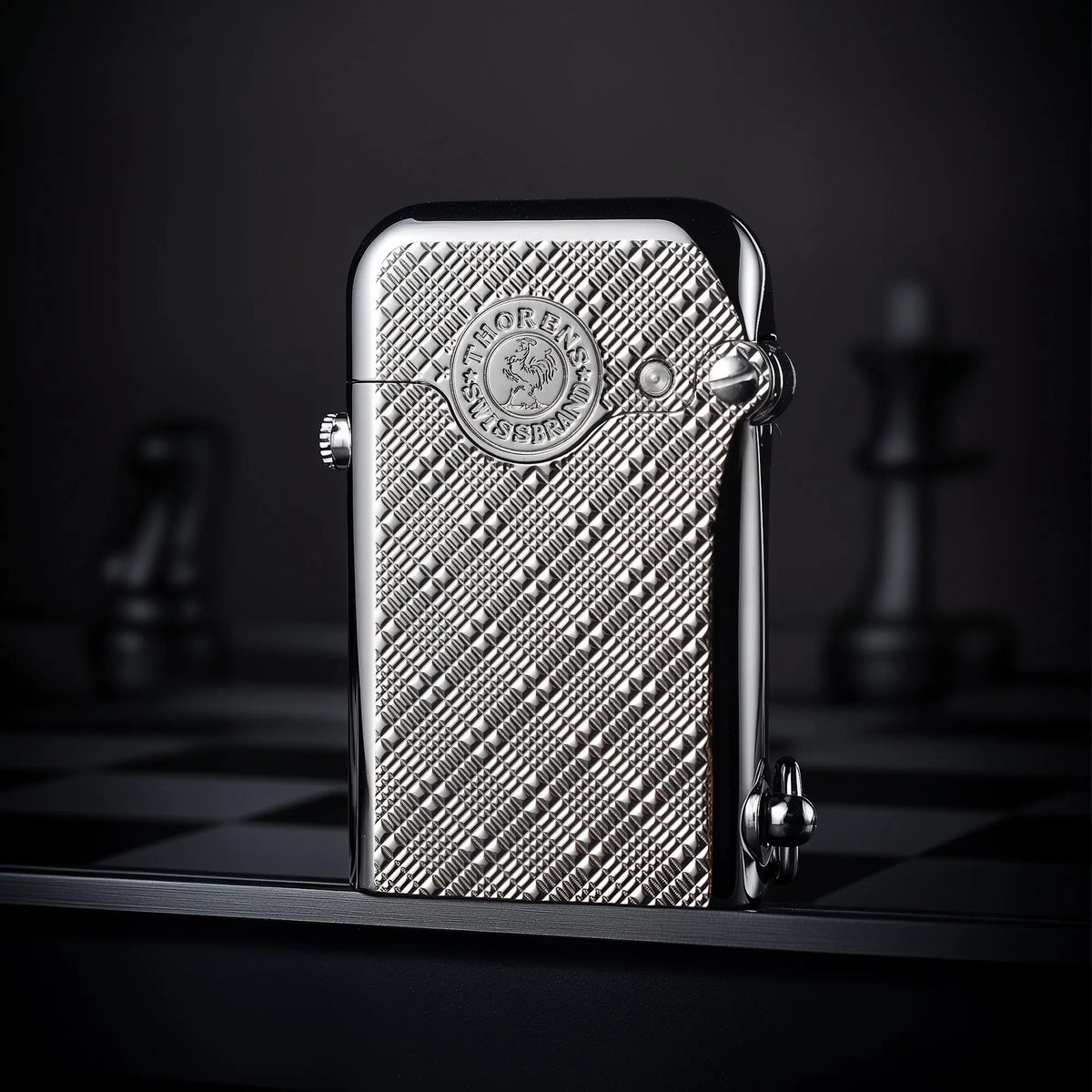 A silver Thorens Gen 1 single claw lighter featuring an intricate engraved plum pattern and heritage brand emblem on a chessboard surface.