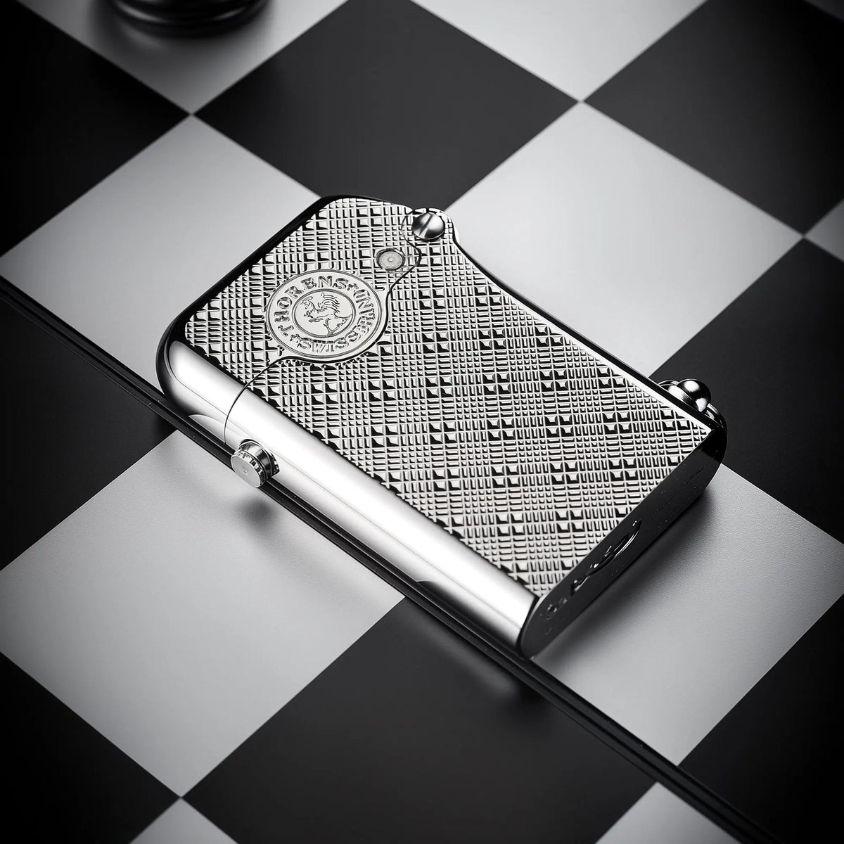 A silver Thorens Gen 1 single claw lighter featuring a detailed plum pattern engraving, resting horizontally on a black and white chessboard.