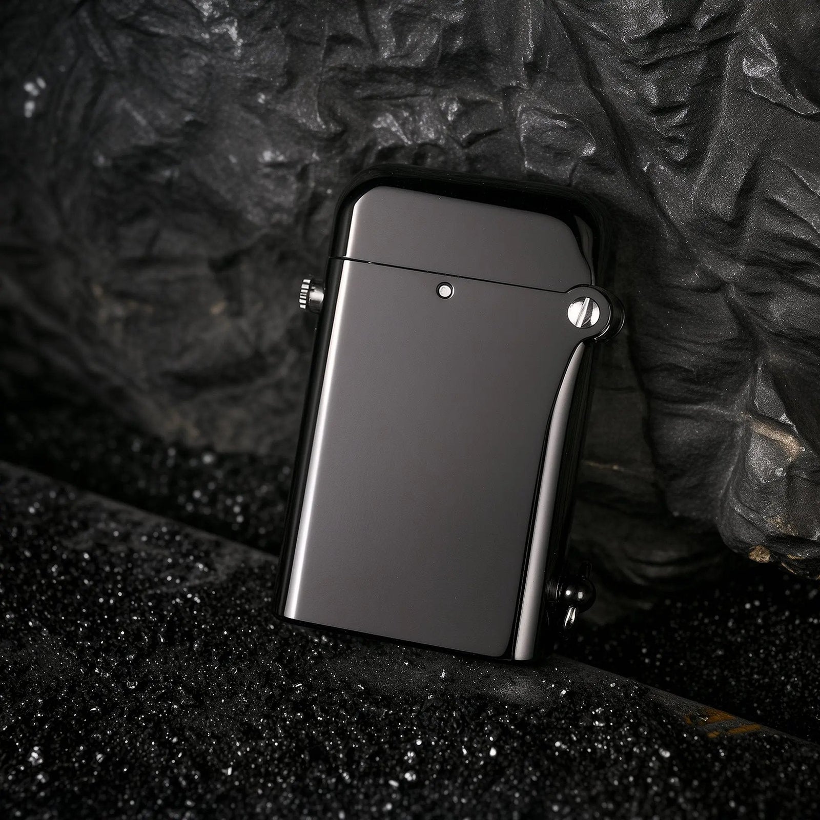 A glossy black Gen 2 Double Claw lighter leaning against a dark, textured rock surface, highlighting the sleek contrast between its polished finish and the rugged outdoor background.