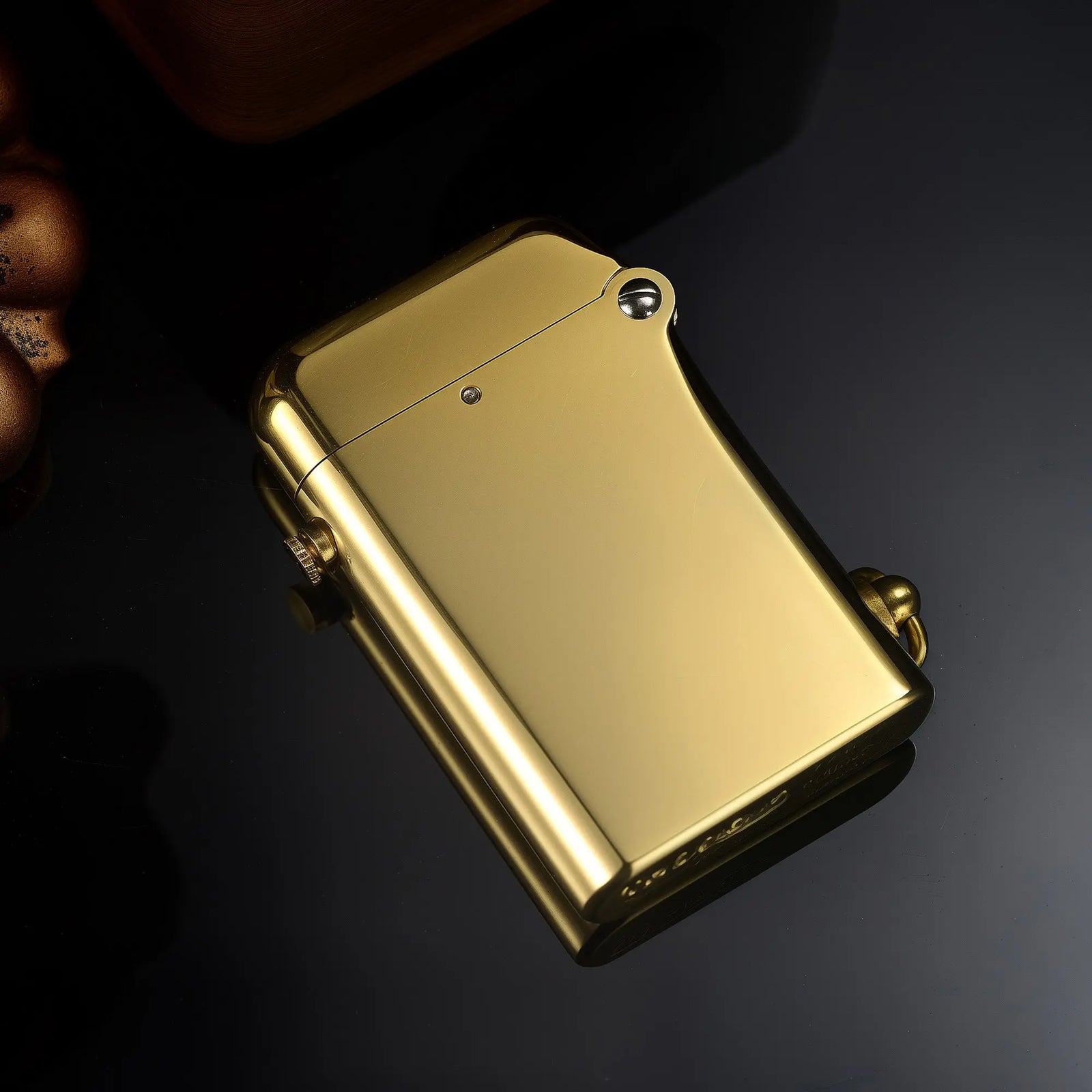 A studio profile view of the closed Gen 2 Double Claw Glossy Brass lighter on a reflective black surface, highlighting its high-polish finish.