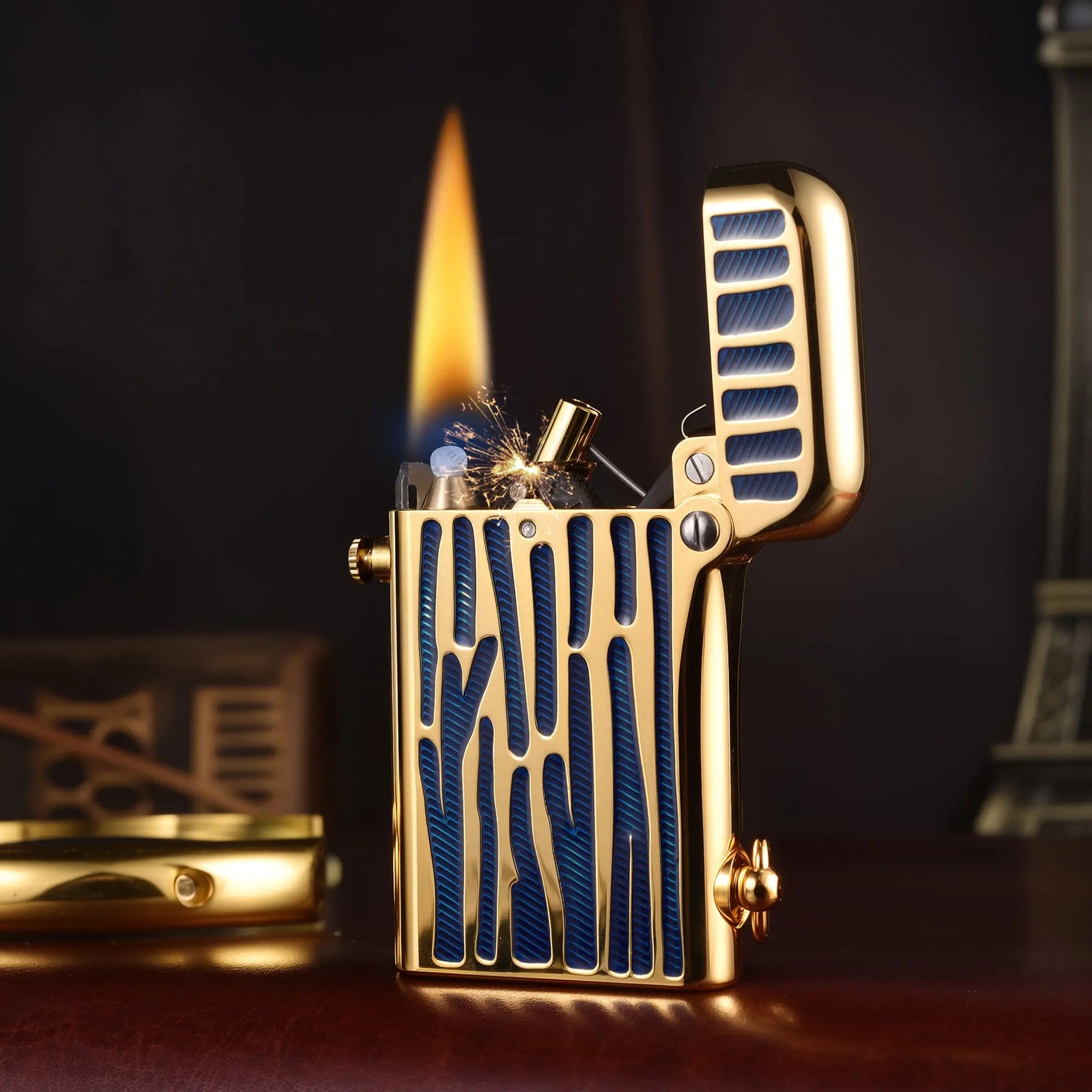 An ignited Thorens Gen 2 Double Claw mechanical lighter in polished gold and blue inlay, showcasing the open dual-claw mechanism, a visible spark, and a steady flame.