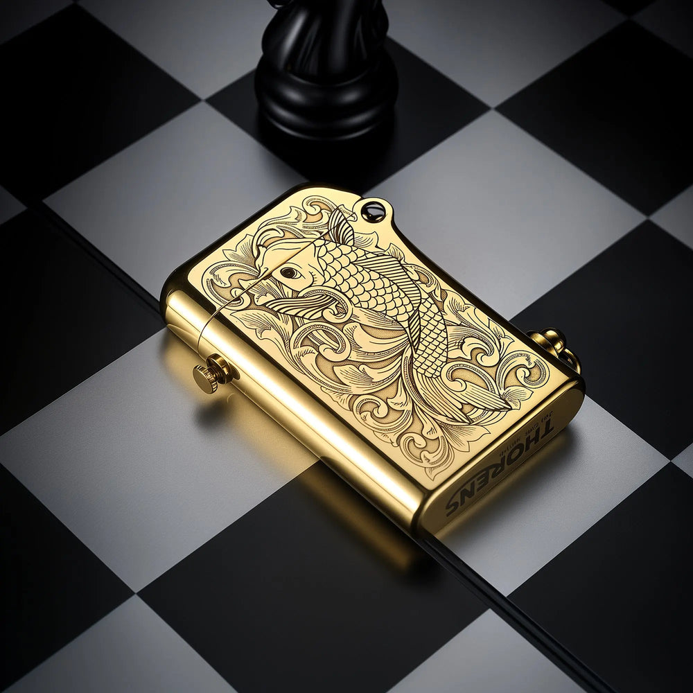 A brass Thorens Gen 2 double claw lighter with an engraved koi fish pattern, resting horizontally on a black and white chessboard.