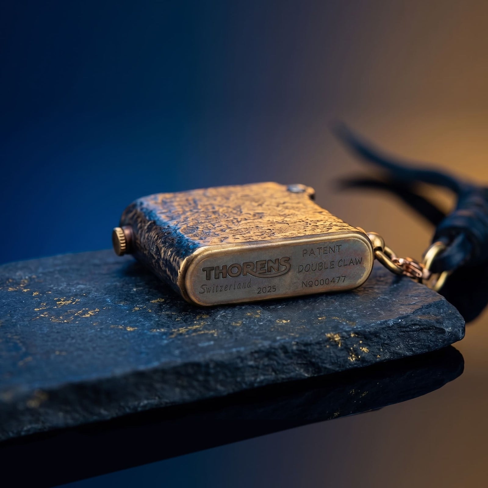 Thorens Gen 2 Double Claw Warhorse lighter resting closed on a stone slab, highlighting the engraved base markings and the side ring connection with attached leather cord.