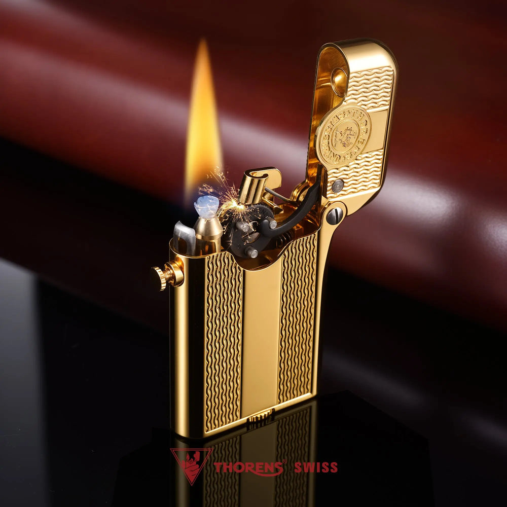 An ignited Thorens Gen 3 gold lighter featuring the spaced water ripple pattern; close-up shows the flint sparks and steady flame against the polished gold lid and branding medallion.