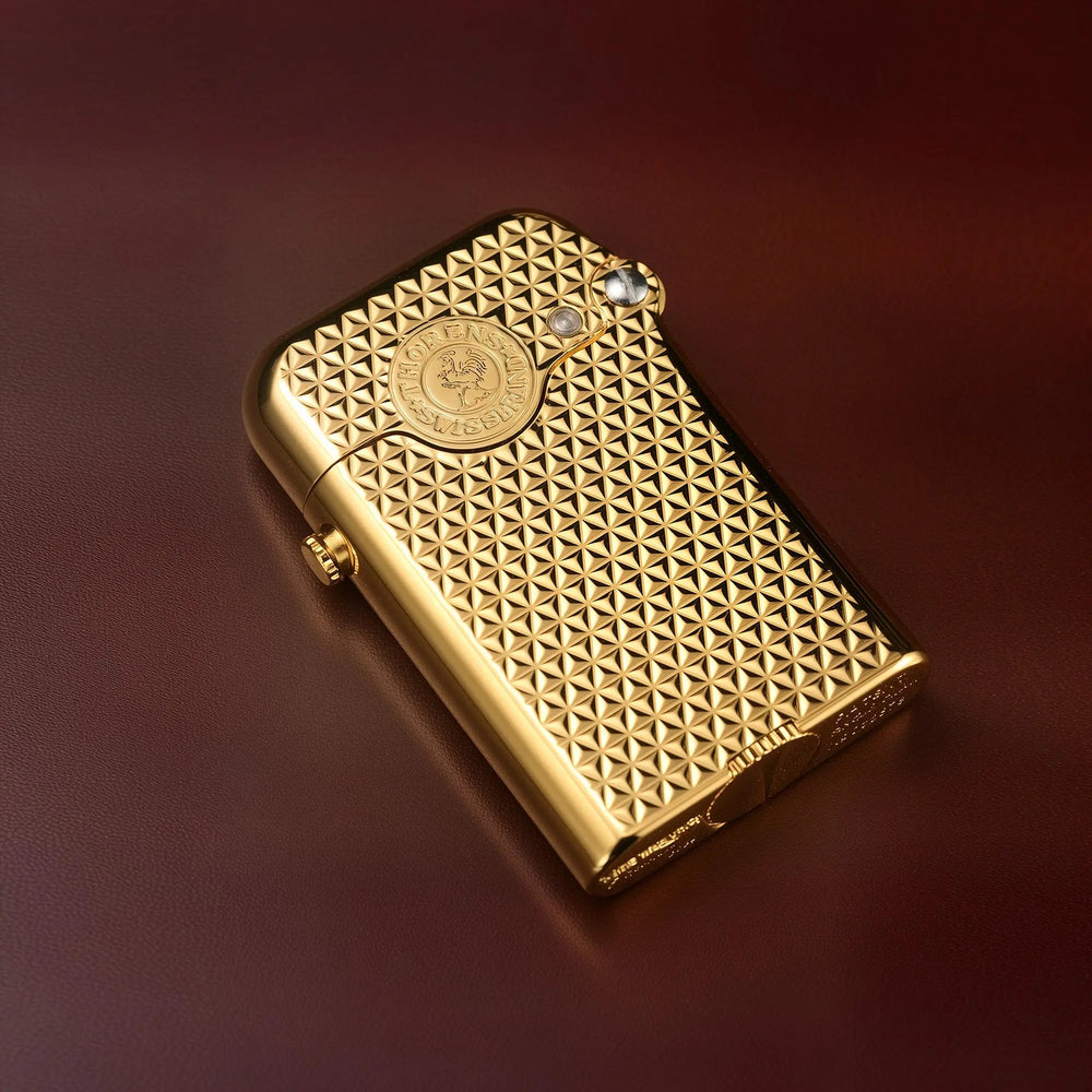 A Thorens Gen 3 gold lighter resting on a leather surface, highlighting the precision-engraved diamond grid texture and signature mechanical hinge.