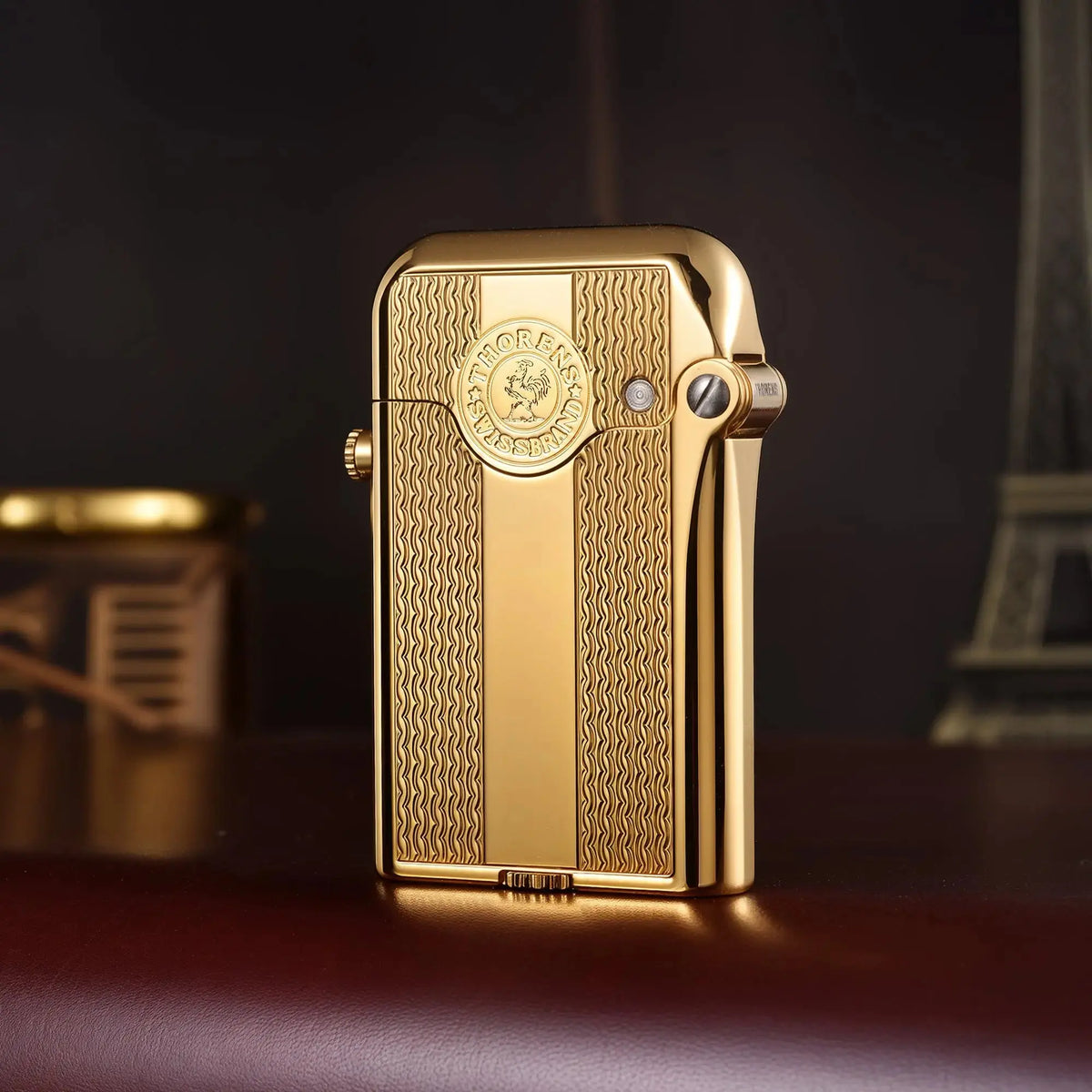 A vertical view of a gold-finished Thorens Gen 3 single claw lighter, showcasing the spaced water ripple engraving and the iconic Thorens circular logo medallion.