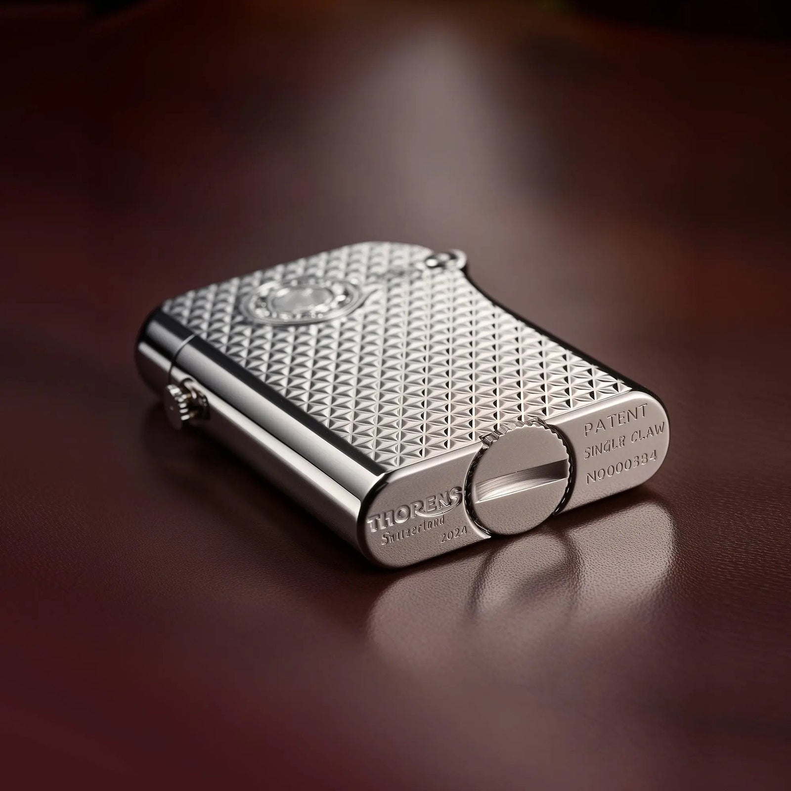 A close-up view of the bottom of the Thorens Gen 3 Diamond Grid silver lighter, showing the detailed patent engravings, serial number, and the textured fuel intake cap against a leather backdrop.