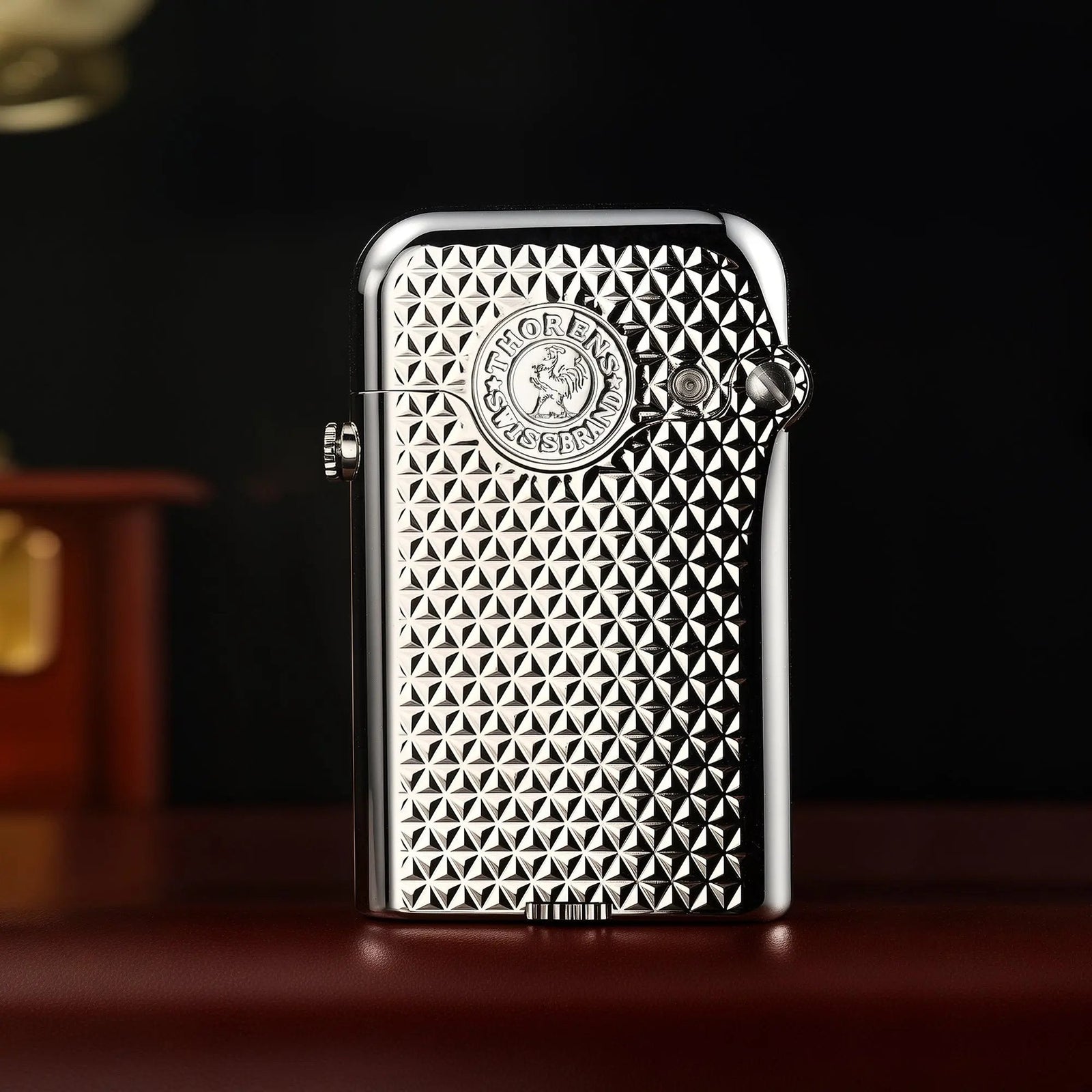A vertical shot of the Thorens Gen 3 Single Claw silver lighter, showcasing the high-reflectivity diamond grid texture and the embossed heritage brand emblem against a dark background.