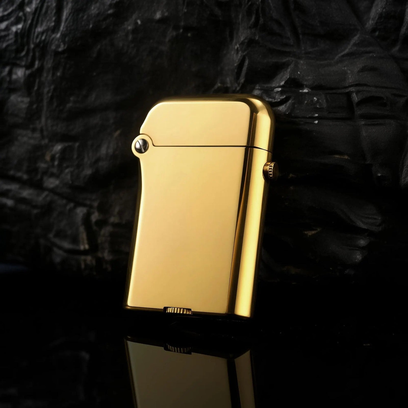 A Thorens Gen 3 Single Claw brass finish lighter with a polished glossy surface, positioned against a dark textured rock background with a sleek reflection.