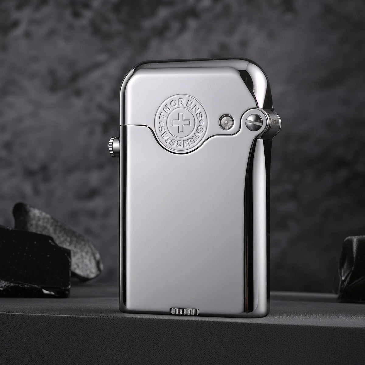 A closed Gen 3 Single Claw silver lighter with a glossy finish and embossed Thorens brand emblem, displayed against a dark stone background.
