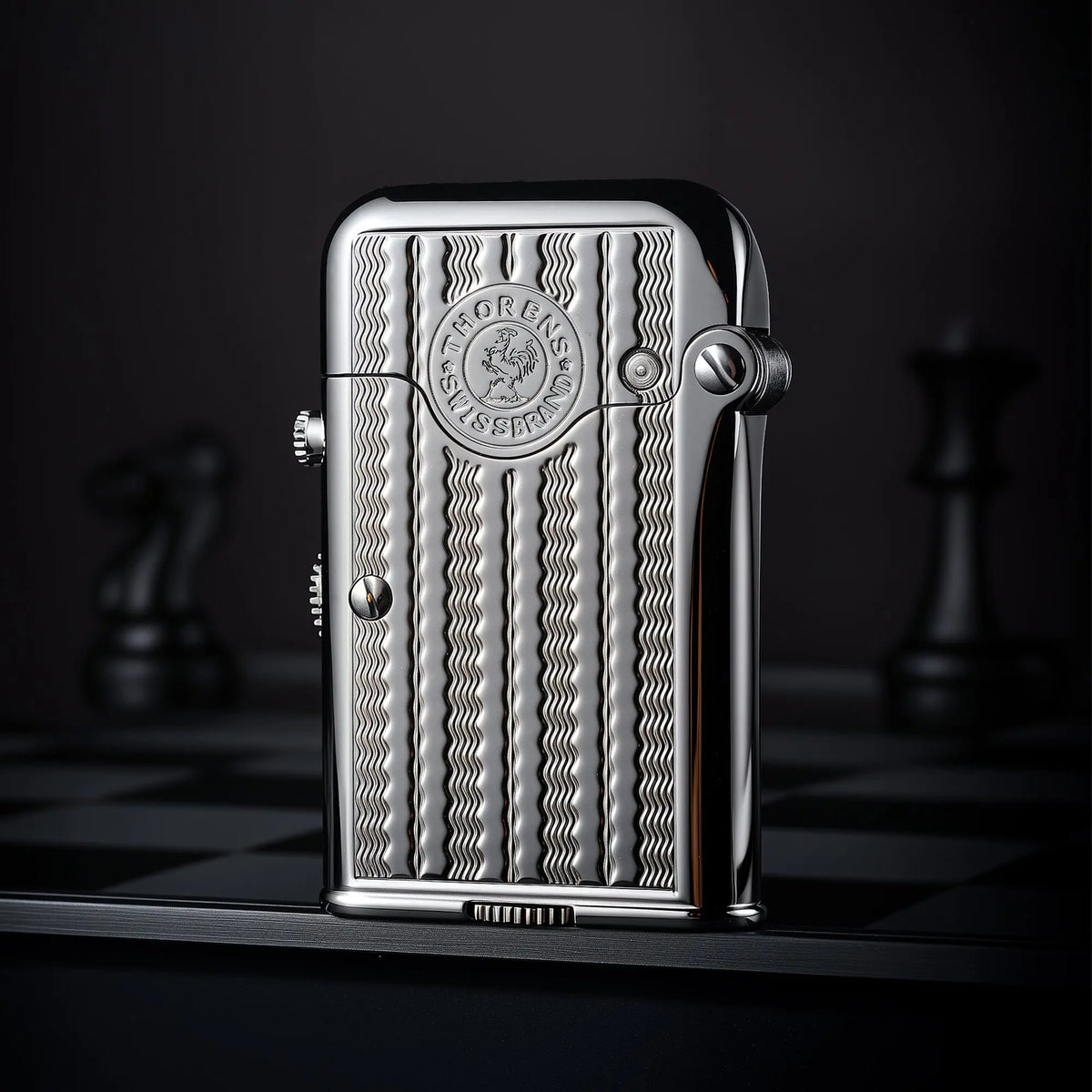 A vertical view of a silver Thorens Gen 7 TELEFLAM lighter featuring a vertical water ripple engraving and heritage emblem on a dark chessboard background.