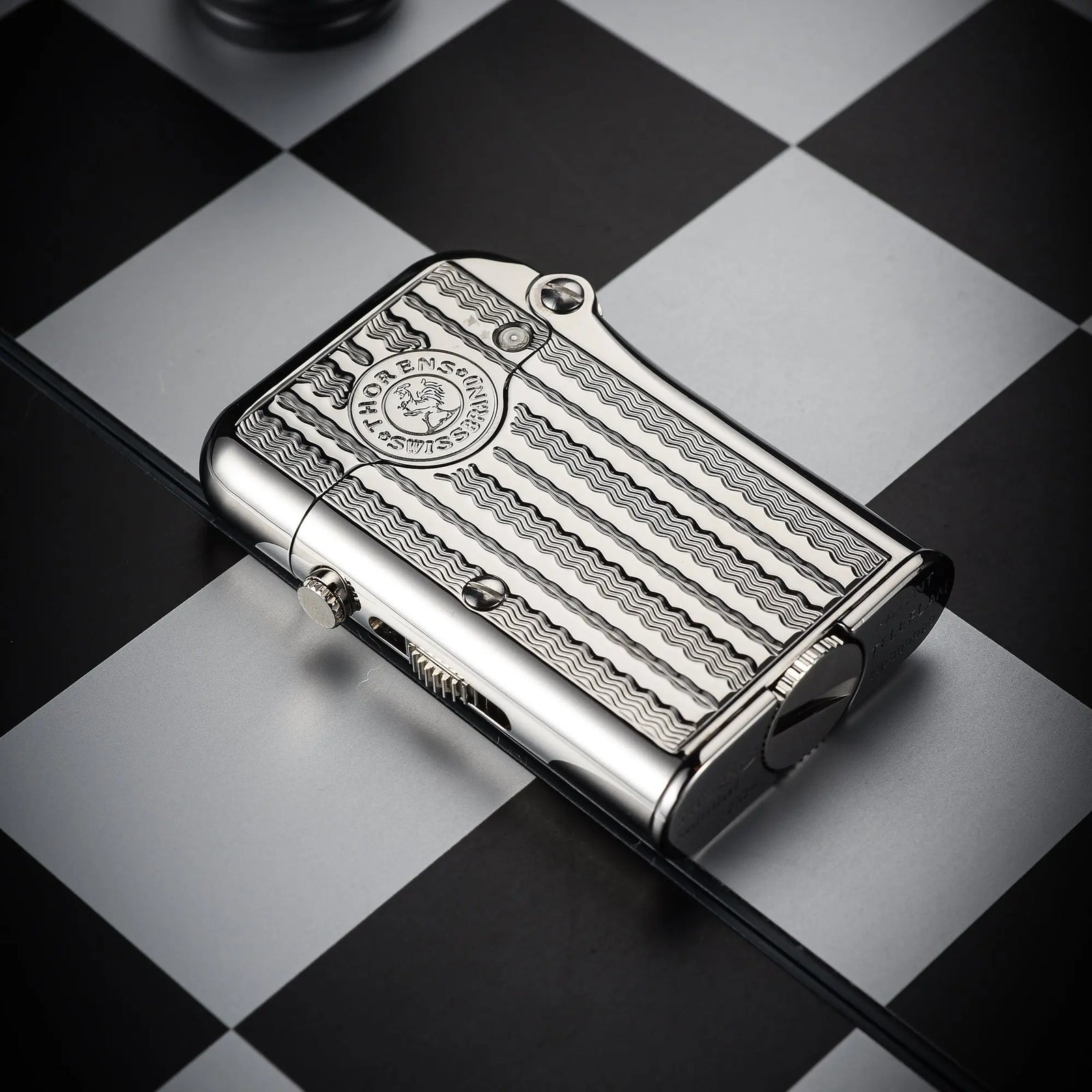 A silver Thorens Gen 7 TELEFLAM lighter featuring an engraved water ripple texture and brand seal, resting horizontally on a black and white chessboard.