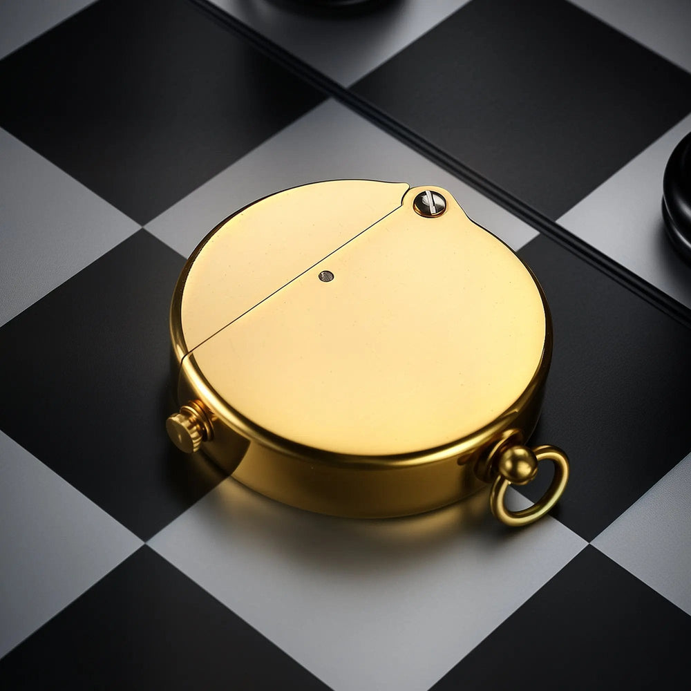A Thorens Gen 8 Double Claw lighter in a polished glossy brass finish, resting on a black and white chessboard, showcasing its smooth circular design.