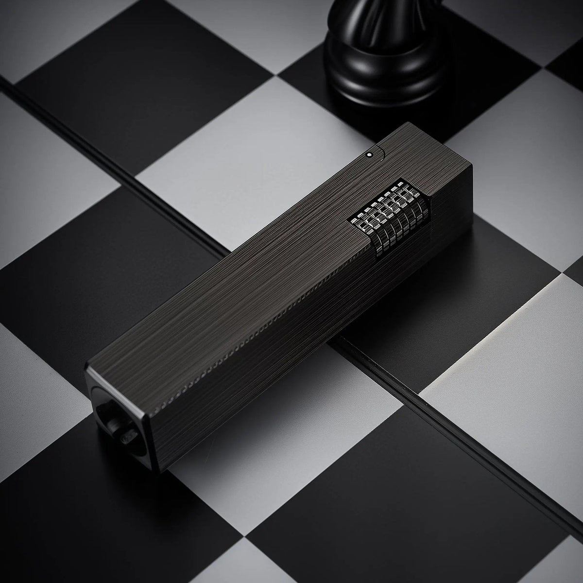 A side view of the Glossy Black Side Slip rectangular lighter with a vertical brushed metal finish and a silver ignition roller on a chessboard.