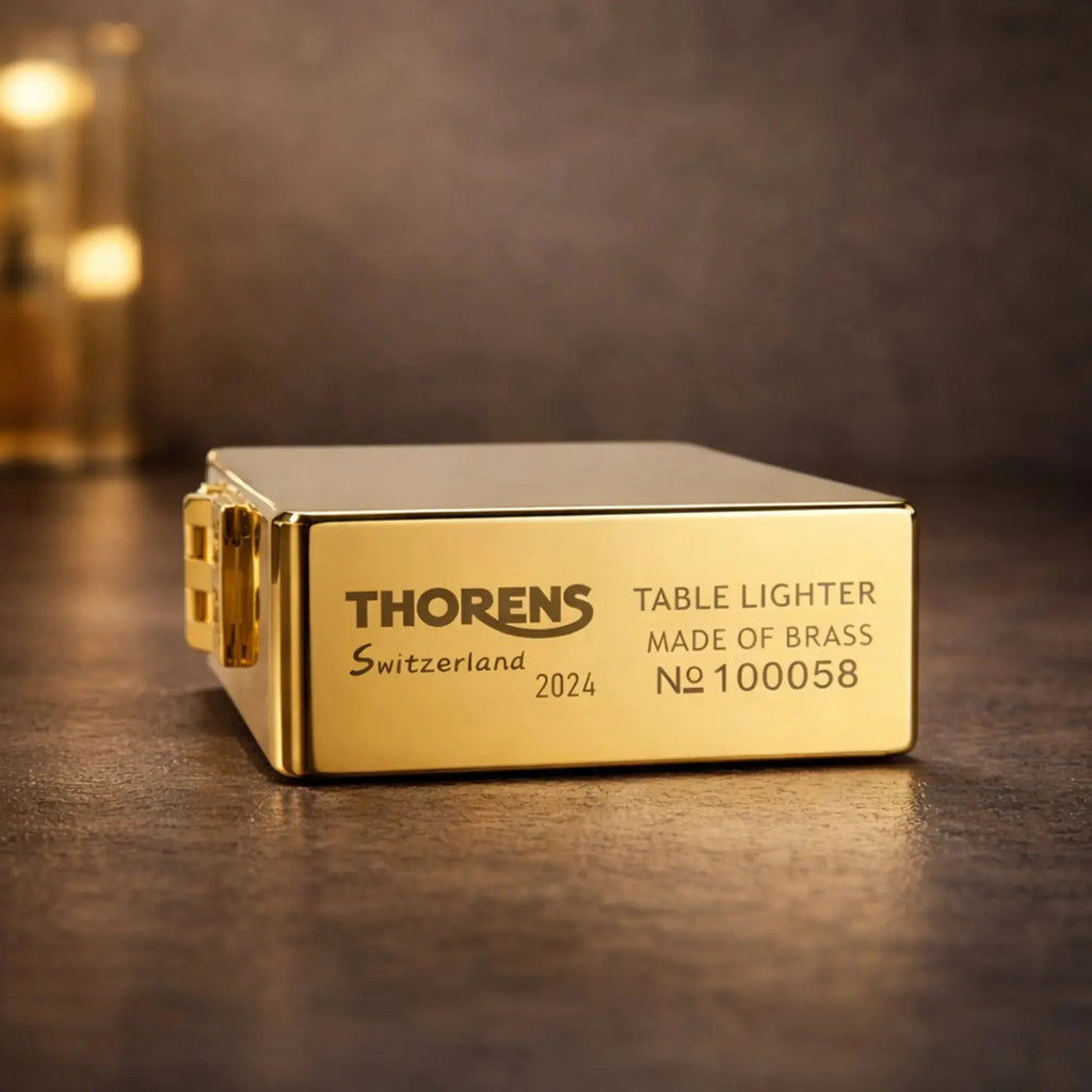 A close-up of the high-polish gold Armor table lighter's base, featuring deep-engraved official branding: "THORENS Switzerland 2024," "TABLE LIGHTER MADE OF BRASS," and a unique serial number for collector authenticity.