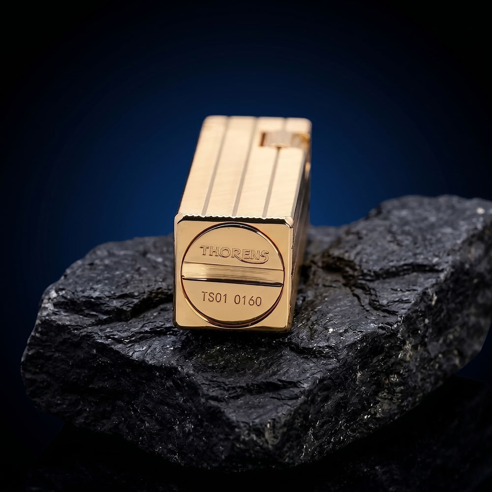 Thorens rectangular lighter with gold diagonal pattern shown on dark stone, highlighting the engraved base logo, serial number, and surface pattern.