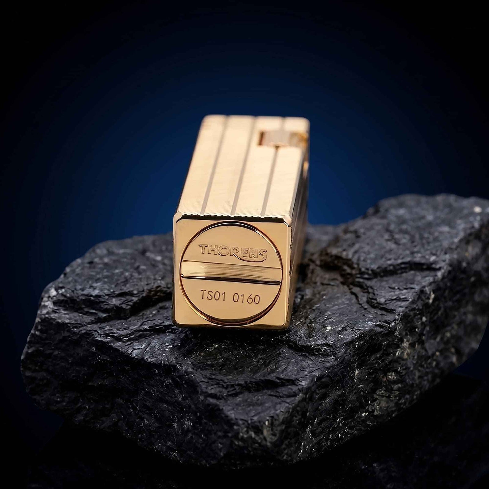 Thorens rectangular lighter with gold diagonal pattern shown on dark stone, highlighting the engraved base logo, serial number, and surface pattern.