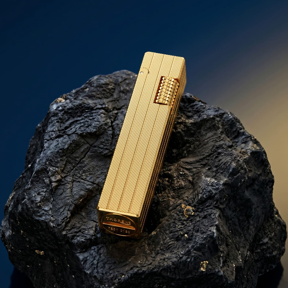 Thorens rectangular lighter with gold diagonal pattern shown with the lid down on dark stone, highlighting the surface pattern and side ignition wheel.