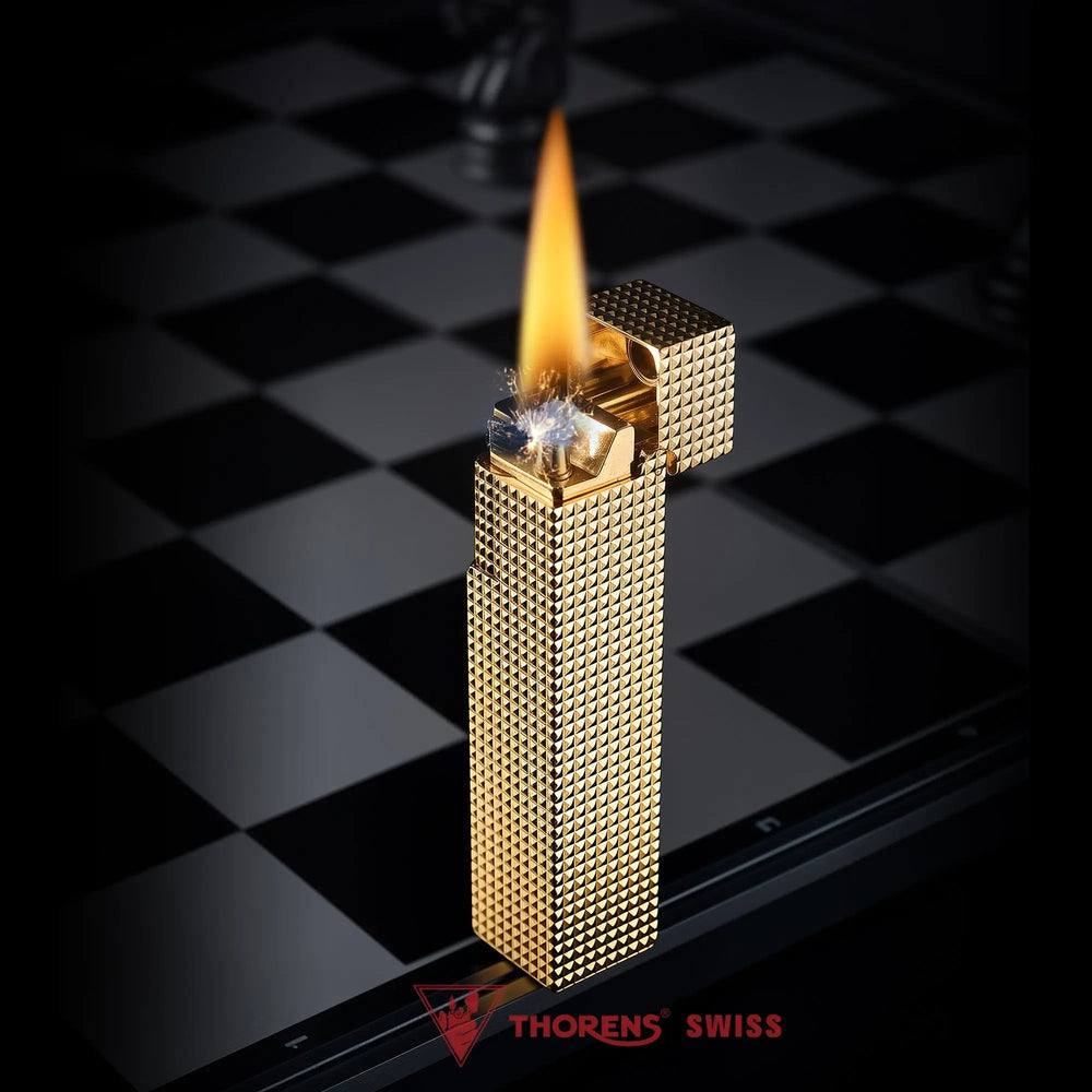 Lit gold small square textured Thorens side-slip rectangular lighter standing open on a black and white checkerboard surface