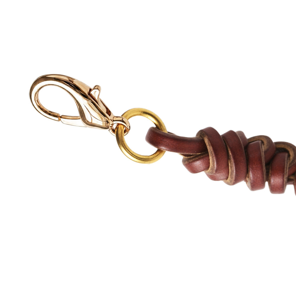 Handwoven cowhide leather charm with braided strap and polished metal clasp and ring, highlighting natural leather texture and fastening detail.