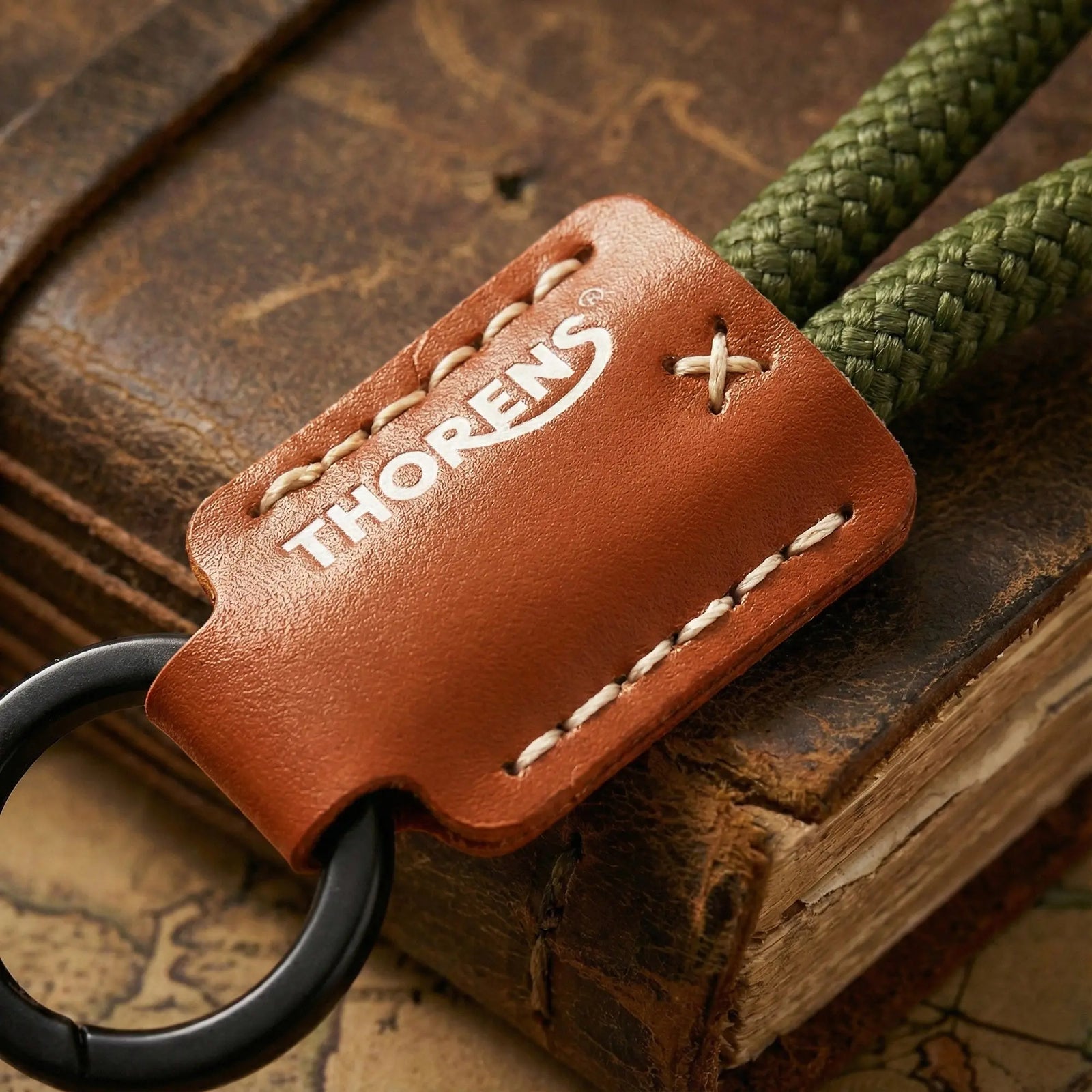 Macro shot of a Thorens keychain featuring a brown leather sleeve with white contrast stitching, resting on an antique leather-bound book.