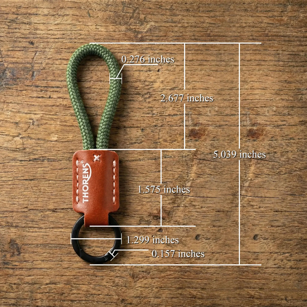 A Thorens keychain with an olive green paracord loop and brown leather sleeve, showing detailed measurements on a wooden surface.