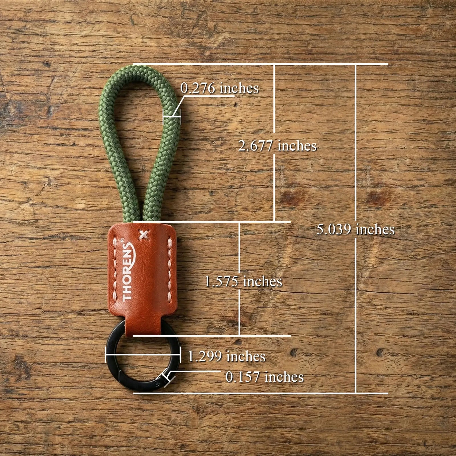 A Thorens keychain with an olive green paracord loop and brown leather sleeve, showing detailed measurements on a wooden surface.