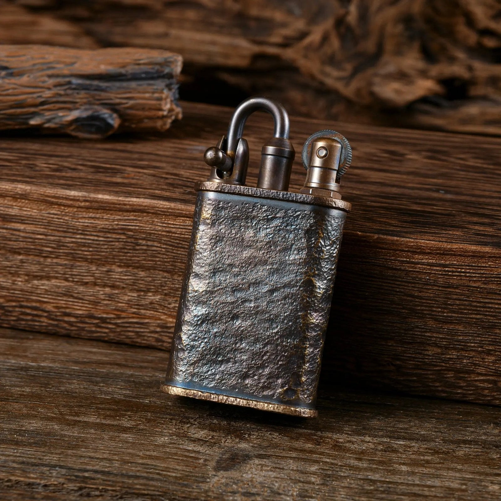 A rugged, antique-style brass lighter with a heavy "Meteorite Crater" hand-carved texture, featuring a distinctive semi-automatic Lockflame ignition system and a weathered patina, resting on a rustic wooden surface.