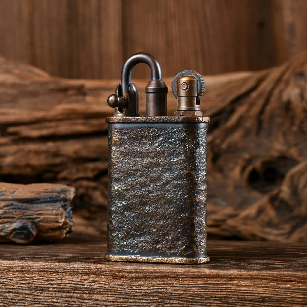 A Thorens Lockflame lighter with a hand-carved meteorite crater texture on a brass body, showcasing mechanical precision and heritage craftsmanship against a rustic wooden backdrop.