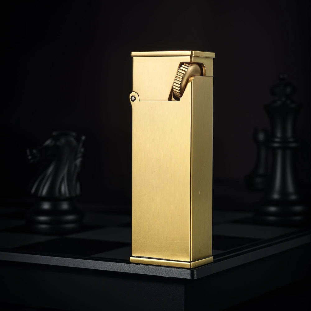 A vertical shot of the Long Fellow lighter in brushed brass, standing on a chessboard to highlight its elongated rectangular body and inclined ignition wheel.