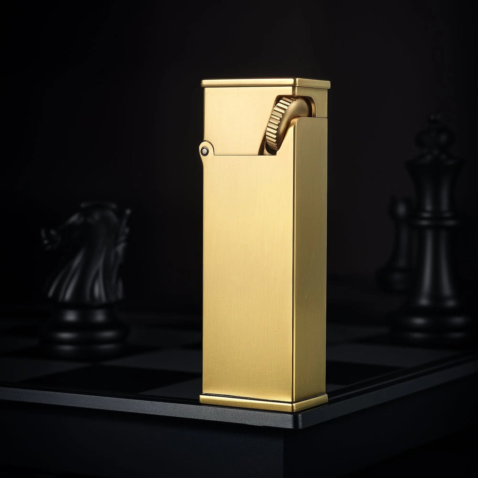 A vertical shot of the Long Fellow lighter in brushed brass, standing on a chessboard to highlight its elongated rectangular body and inclined ignition wheel.