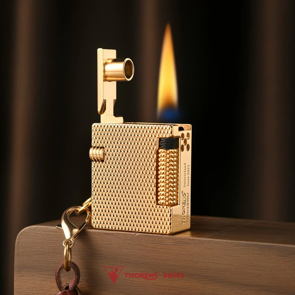 A lit Mini Cube Golden Mesh lighter with an upright mechanical arm and steady flame, showcasing its brass textured body on a wooden block.