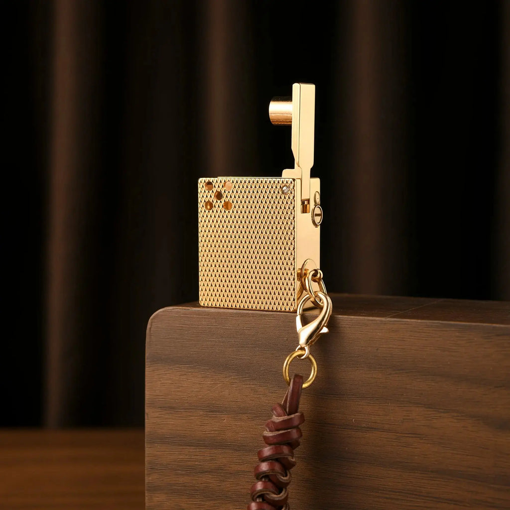 A Mini Cube Golden Mesh lighter with an open mechanical arm and leather lanyard, standing on a wooden surface against a dark background.