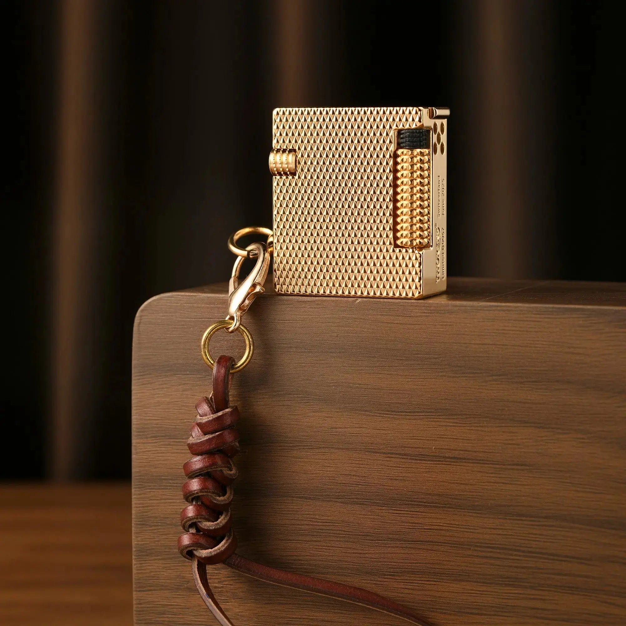 A Mini Cube Golden Mesh lighter with intricate brass engraving and a leather lanyard, standing upright on a walnut wood block.