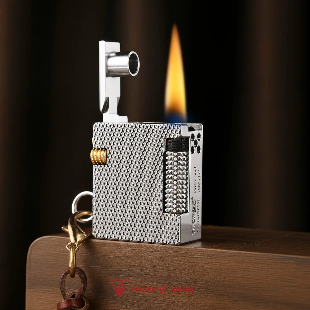 A lit Thorens Mini Cube Silver Mesh lighter standing on wood, showing the ignited flame, open lid mechanism, and intricate textured metal finish.