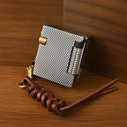 A Thorens Mini Cube lighter in silver mesh finish, shown closed on a wooden surface with a braided brown leather lanyard and brass hardware.